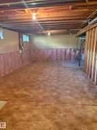 Unfinished basement featuring exposed wood joists, a carpeted floor, and partial wall insulation - 
