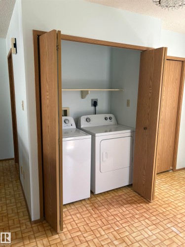 In-unit laundry facilities featuring a white washer and dryer, bifold wood-finish doors, and a utility shelf - 17520 Callingwood Road Nw, Edmonton, AB - Indoor Photo Showing Laundry Room
