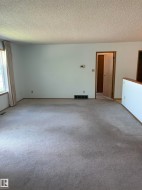 Spacious interior room featuring light-colored wall-to-wall carpeting, white walls, and a window with drapery - 