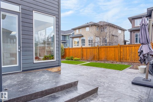 Expansive stamped concrete patio with two steps, artificial turf accents, and a wood privacy fence - 1313 Hainstock Way Sw, Edmonton, AB - Outdoor
