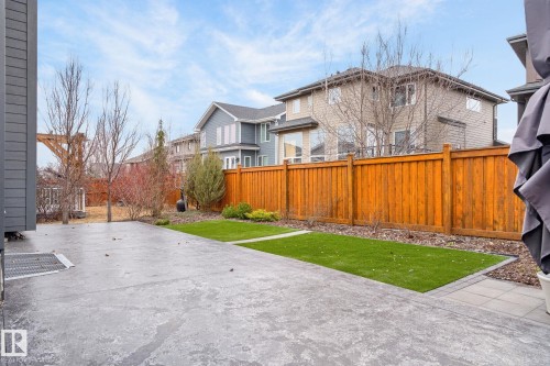 Spacious patio area featuring stamped concrete, a strip of artificial turf, and a wood privacy fence - 1313 Hainstock Way Sw, Edmonton, AB - Outdoor