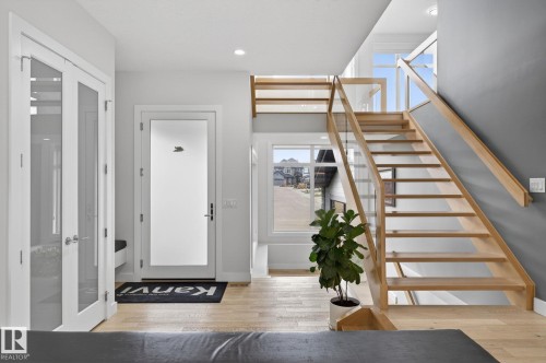 Open-tread staircase with wood-finish steps and glass railing, complemented by hardwood flooring - 1313 Hainstock Way Sw, Edmonton, AB - Indoor Photo Showing Other Room