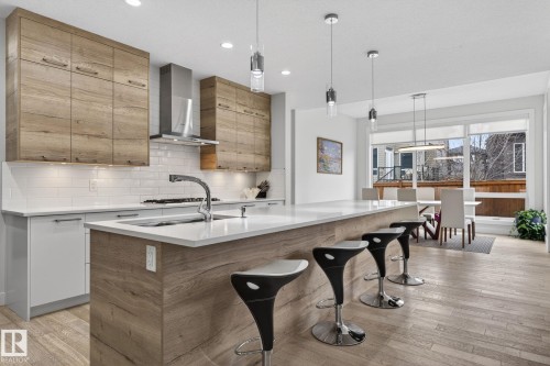 Contemporary kitchen featuring an expansive center island with seating, integrated sink, and wood-finish paneling - 1313 Hainstock Way Sw, Edmonton, AB - Indoor Photo Showing Kitchen With Upgraded Kitchen