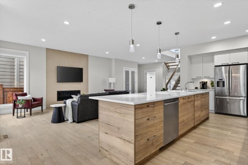 Open-concept living space featuring a large kitchen island with a white countertop, recessed lighting, wood-finish flooring, a contemporary fireplace, and a staircase with open risers - 1313 Hainstock Way Sw, Edmonton, AB - Indoor Photo Showing Kitchen With Upgraded Kitchen