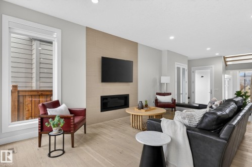 Living area featuring wood-finish flooring, recessed lighting, and a modern fireplace with a light-toned accent wall - 1313 Hainstock Way Sw, Edmonton, AB - Indoor Photo Showing Living Room With Fireplace
