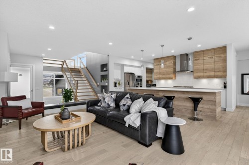 Open-concept living area featuring light wood-finish flooring, recessed lighting, and a modern staircase with glass railings - 1313 Hainstock Way Sw, Edmonton, AB - Indoor Photo Showing Living Room