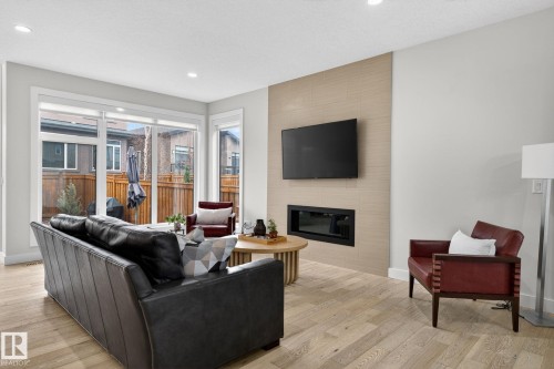 Living area featuring wood-finish flooring, recessed lighting, and a linear fireplace set within a textured accent wall - 1313 Hainstock Way Sw, Edmonton, AB - Indoor Photo Showing Living Room With Fireplace