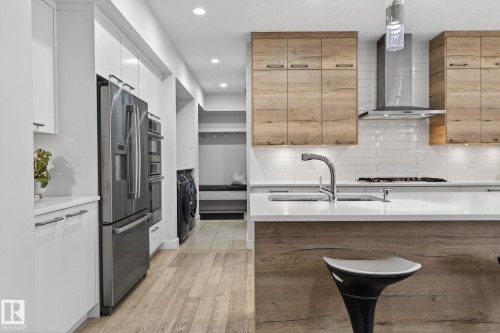 Gourmet kitchen featuring a central island with integrated sink, stainless steel appliances, wood-finish flooring, white subway tile backsplash, and recessed lighting - 1313 Hainstock Way Sw, Edmonton, AB - Indoor Photo Showing Kitchen With Upgraded Kitchen