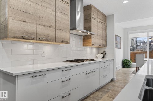 Modern kitchen featuring wood-finish upper cabinetry, a stainless steel range hood, and a gas cooktop - 1313 Hainstock Way Sw, Edmonton, AB - Indoor Photo Showing Kitchen With Upgraded Kitchen