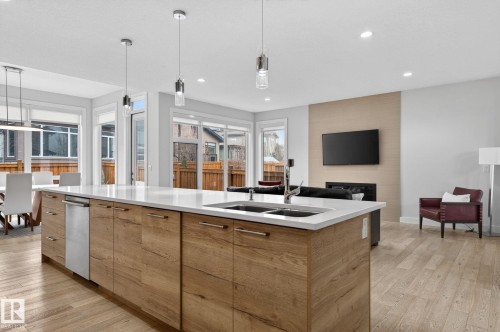 Kitchen island with wood-finish cabinetry, white countertop, and integrated double basin sink - 1313 Hainstock Way Sw, Edmonton, AB - Indoor Photo Showing Kitchen With Double Sink