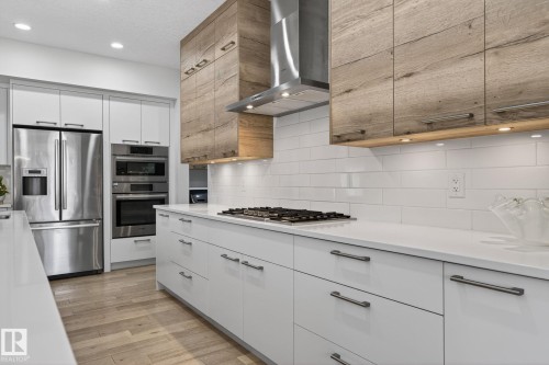 Modern kitchen featuring light wood-finish flooring, white flat-panel cabinetry with dark hardware, stainless steel appliances, a gas range, and white subway tile backsplash - 1313 Hainstock Way Sw, Edmonton, AB - Indoor Photo Showing Kitchen With Upgraded Kitchen