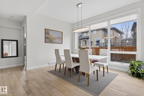 Dining area featuring extensive natural light, light wood-finish flooring, a modern linear pendant light fixture, and white trim - 1313 Hainstock Way Sw, Edmonton, AB - Indoor Photo Showing Dining Room