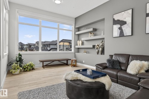Living area featuring expansive windows, light wood-finish flooring, recessed wall shelving, and a neutral color palette - 1313 Hainstock Way Sw, Edmonton, AB - Indoor Photo Showing Living Room