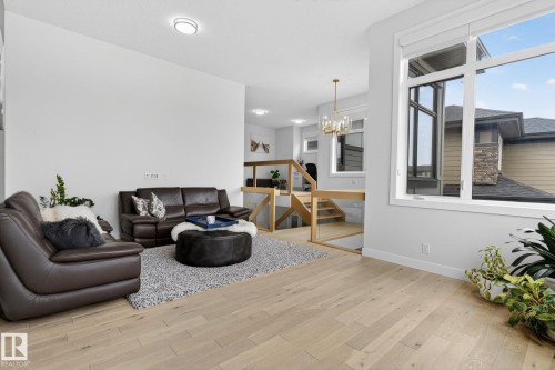 Bright open-concept living area featuring light wood-finish flooring, a large multi-pane window, and a contemporary chandelier - 1313 Hainstock Way Sw, Edmonton, AB - Indoor Photo Showing Other Room
