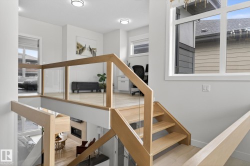 Light wood-finish staircase with glass panel railing and matching second-story landing overlooking a lower level - 1313 Hainstock Way Sw, Edmonton, AB - Indoor Photo Showing Other Room
