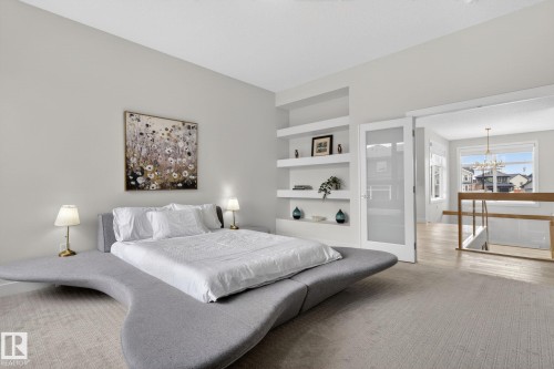 Carpeted room featuring built-in shelving, a full-light French door with frosted glass, and a wide entryway to a space with wood-finish flooring and a staircase with a wood and glass railing - 1313 Hainstock Way Sw, Edmonton, AB - Indoor Photo Showing Bedroom