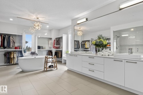 Spacious bathroom featuring a freestanding tub, dual vessel sinks, extensive built-in cabinetry, glass-enclosed shower, and a decorative chandelier - 1313 Hainstock Way Sw, Edmonton, AB - Indoor Photo Showing Bathroom