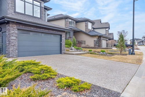 Modern two-story home featuring a stone facade, a gray sectional garage door, large upper-level windows, and a concrete driveway - 1313 Hainstock Way Sw, Edmonton, AB - Outdoor