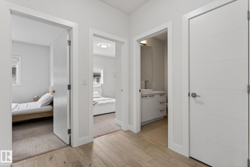 Hallway with light wood-finish flooring featuring three doorways - 1313 Hainstock Way Sw, Edmonton, AB - Indoor