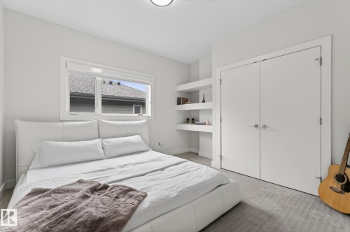 Bright interior space featuring a window with white trim, built-in shelving, white bi-fold closet doors, and patterned carpeting - 1313 Hainstock Way Sw, Edmonton, AB - Indoor Photo Showing Bedroom