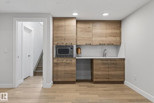 Built-in wood-finish cabinetry featuring a microwave, sink with a chrome faucet, and white subway tile backsplash - 1313 Hainstock Way Sw, Edmonton, AB - Indoor