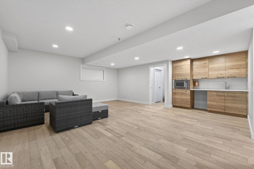 Spacious room featuring wood-finish flooring, recessed lighting, a window with blinds, and a built-in wet bar with wood cabinetry, a sink, and an integrated microwave - 1313 Hainstock Way Sw, Edmonton, AB - Indoor