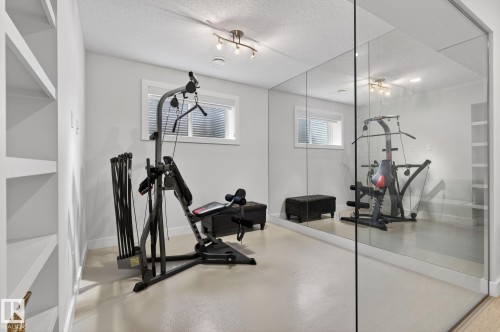 Dedicated fitness room featuring a full-length mirrored wall, a window with horizontal blinds, built-in shelving, and recessed lighting - 1313 Hainstock Way Sw, Edmonton, AB - Indoor Photo Showing Gym Room