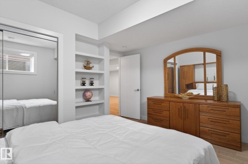 Bedroom featuring built-in shelving, mirrored closet doors, a window with blinds, and white walls - 1313 Hainstock Way Sw, Edmonton, AB - Indoor Photo Showing Bedroom