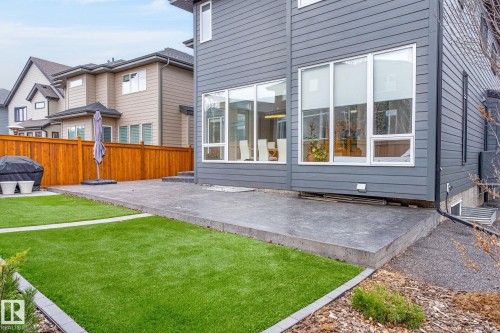 Gray horizontal siding exterior with large windows, a concrete patio, a wood fence, and a manicured lawn - 1313 Hainstock Way Sw, Edmonton, AB - Outdoor With Deck Patio Veranda