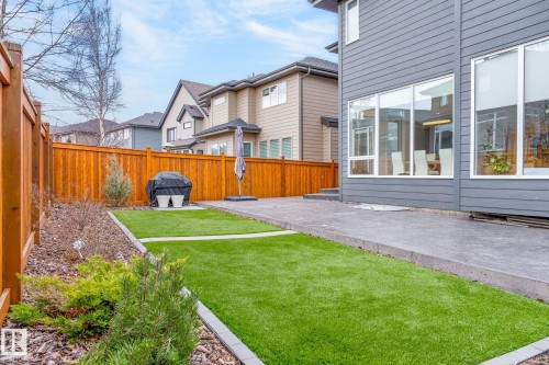 Backyard featuring a privacy fence, artificial turf, concrete patio, and garden beds - 1313 Hainstock Way Sw, Edmonton, AB - Outdoor
