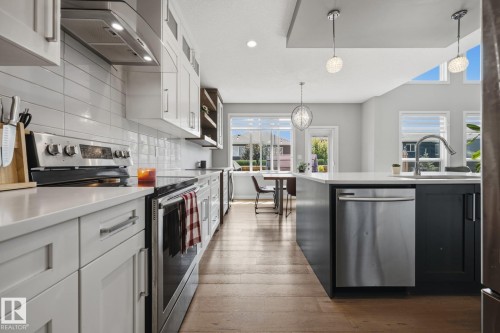 Modern kitchen featuring white shaker cabinetry, stainless steel appliances, a tile backsplash, and wood-finish flooring - 3870 Robins Crescent Nw, Edmonton, AB - Indoor Photo Showing Kitchen With Upgraded Kitchen