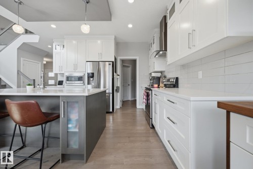 Modern kitchen featuring white shaker cabinetry, stainless steel appliances, a center island with pendant lighting, light wood-finish flooring, and a white subway tile backsplash - 3870 Robins Crescent Nw, Edmonton, AB - Indoor Photo Showing Kitchen With Upgraded Kitchen