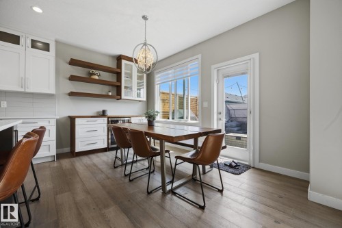 Bright dining space featuring wood-finish flooring, a contemporary chandelier, and large windows with a glass-paneled door - 3870 Robins Crescent Nw, Edmonton, AB - Indoor Photo Showing Dining Room