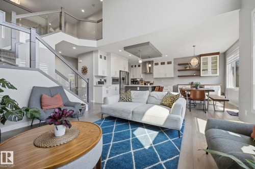 Open-concept living space featuring wood-finish flooring, a contemporary staircase with glass railings, a kitchen with white cabinetry and stainless steel appliances, a dining area with built-in shelving, and recessed lighting - 3870 Robins Crescent Nw, Edmonton, AB - Indoor Photo Showing Living Room