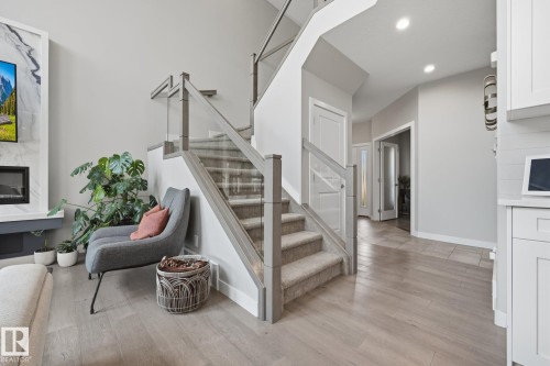 Contemporary staircase featuring glass railings with light wood-finish posts and carpeted treads - 3870 Robins Crescent Nw, Edmonton, AB - Indoor With Fireplace