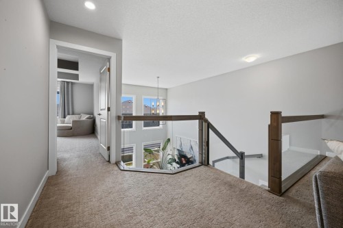 Carpeted hallway featuring a clear glass railing overlooking a lower level, recessed lighting, and a doorway leading to an additional space with windows - 3870 Robins Crescent Nw, Edmonton, AB - Indoor Photo Showing Other Room