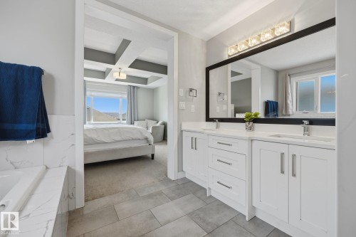 Dual vanity with white cabinetry, integrated sinks, chrome fixtures, and a large framed mirror - 3870 Robins Crescent Nw, Edmonton, AB - Indoor Photo Showing Bathroom