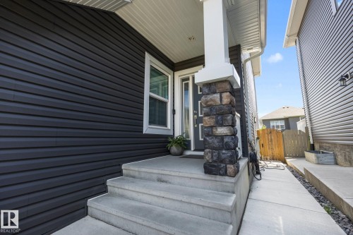 Front entry featuring a stone-clad column, concrete steps, and dark horizontal siding - 3870 Robins Crescent Nw, Edmonton, AB - Outdoor With Exterior