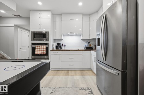 Contemporary kitchen featuring white high-gloss cabinetry, stainless steel appliances, wood-finish countertops, subway tile backsplash, and light wood-finish flooring - 3870 Robins Crescent Nw, Edmonton, AB - Indoor Photo Showing Kitchen With Upgraded Kitchen