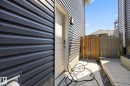 Exterior access area featuring dark horizontal siding, a light-colored entry door, a wrought iron wall sconce, and a wood privacy gate - 3870 Robins Crescent Nw, Edmonton, AB  - Outdoor With Exterior 