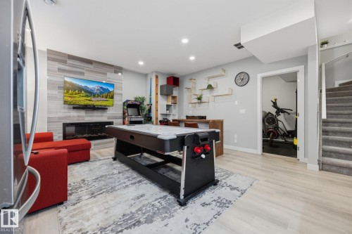 Spacious lower-level entertainment space featuring a light wood-finish flooring, recessed lighting, and a textured accent wall with an integrated fireplace and television mount - 3870 Robins Crescent Nw, Edmonton, AB - Indoor