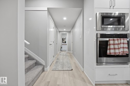 Integrated stainless steel microwave and wall oven with light wood-finish flooring, a carpeted staircase, and recessed lighting throughout - 3870 Robins Crescent Nw, Edmonton, AB - Indoor Photo Showing Other Room
