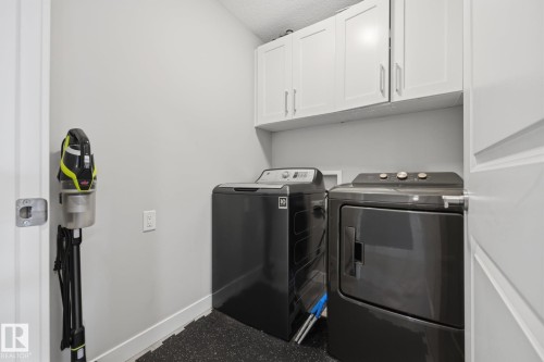 Dedicated laundry area featuring white upper cabinetry, light gray wall paint, and durable black flooring  UPSTAIRS LAUNDRY - 3870 Robins Crescent Nw, Edmonton, AB - Indoor Photo Showing Laundry Room