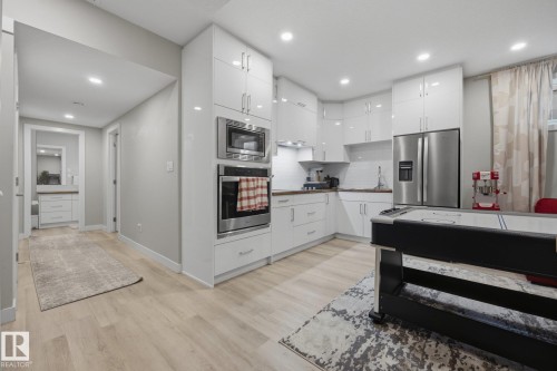 Modern kitchen featuring white glossy cabinetry, stainless steel appliances including a built-in microwave and oven, a stainless steel refrigerator, and wood-finish countertops - 3870 Robins Crescent Nw, Edmonton, AB - Indoor Photo Showing Kitchen