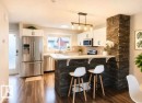 Modern kitchen featuring stainless steel appliances, white cabinetry, wood-finish flooring, a stone-clad island with a breakfast bar, and a contemporary linear pendant light fixture - 225 51A Street Sw, Edmonton, AB  - Indoor 