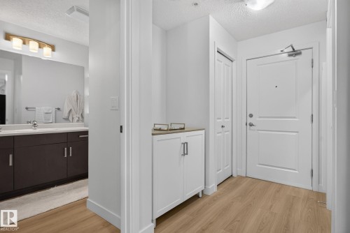 Entryway featuring wood-finish flooring, white panel doors, and a built-in storage cabinet with a light-toned countertop - #203 5521 7 Av Sw, Edmonton, AB - Indoor