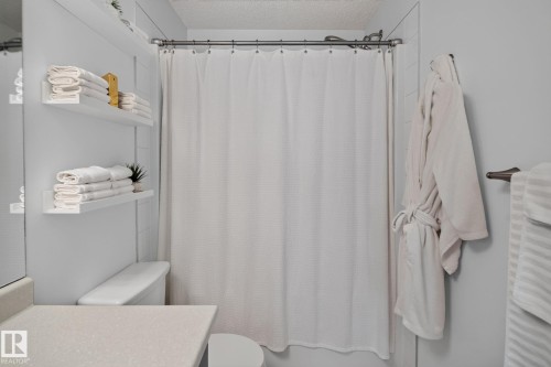 Full bathroom featuring a shower with a white textured curtain, a toilet, and a vanity with a light-toned countertop - #203 5521 7 Av Sw, Edmonton, AB - Indoor Photo Showing Bathroom