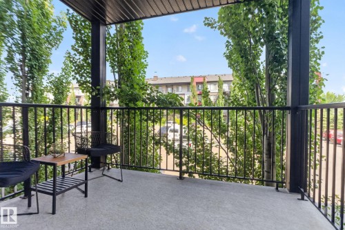 Private balcony featuring textured concrete flooring, black metal railings, and a contrasting dark soffit - #203 5521 7 Av Sw, Edmonton, AB - Outdoor With Balcony With Exterior