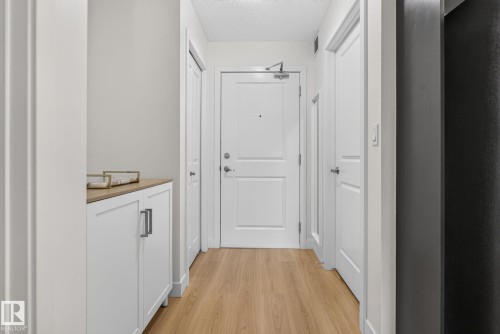 Entryway featuring wood-finish flooring, white paneled doors, and a built-in cabinet with a wood-finish top and brushed nickel hardware - #203 5521 7 Av Sw, Edmonton, AB - Indoor Photo Showing Other Room