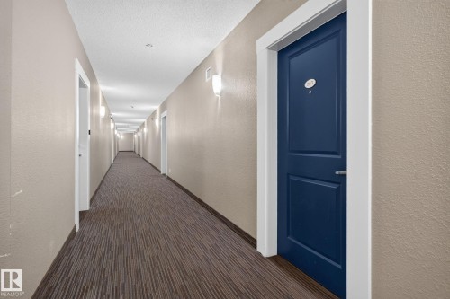 Hallway featuring patterned carpet flooring, neutral-toned textured walls, and a series of wall-mounted sconces - #203 5521 7 Av Sw, Edmonton, AB - Indoor Photo Showing Other Room